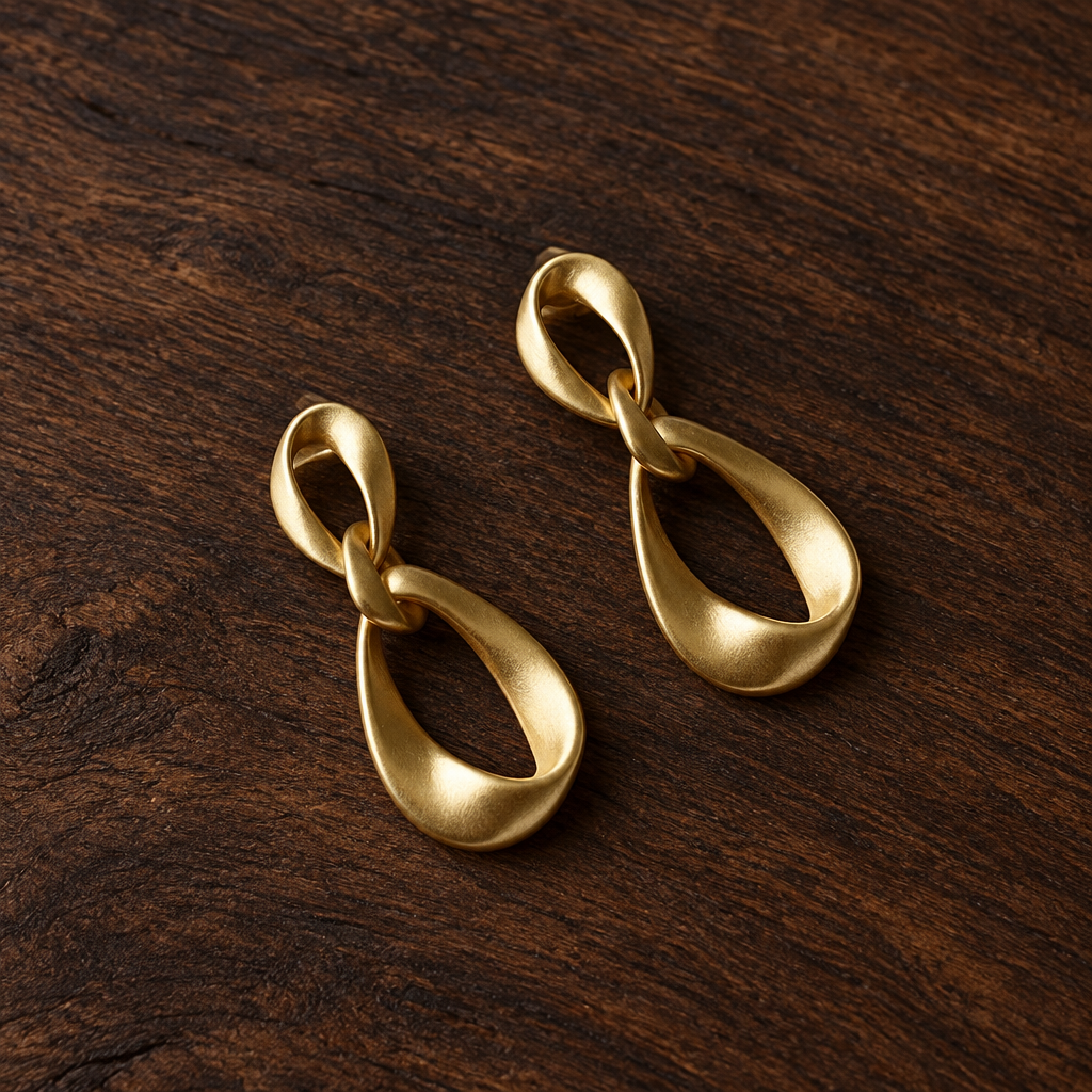 Pair of matte gold-tone geometric teardrop earrings on dark wood