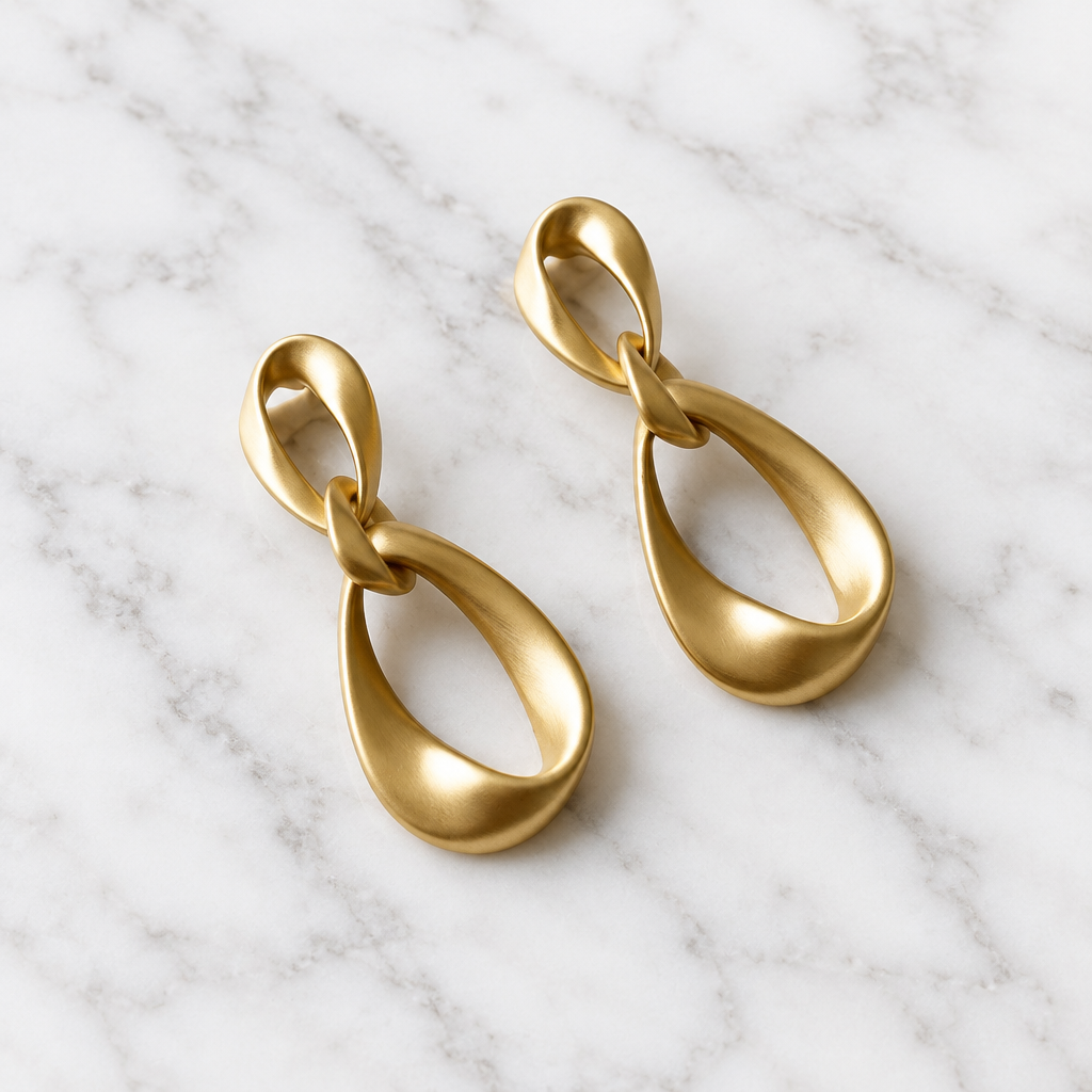 Pair of matte gold-tone geometric teardrop earrings on white marble