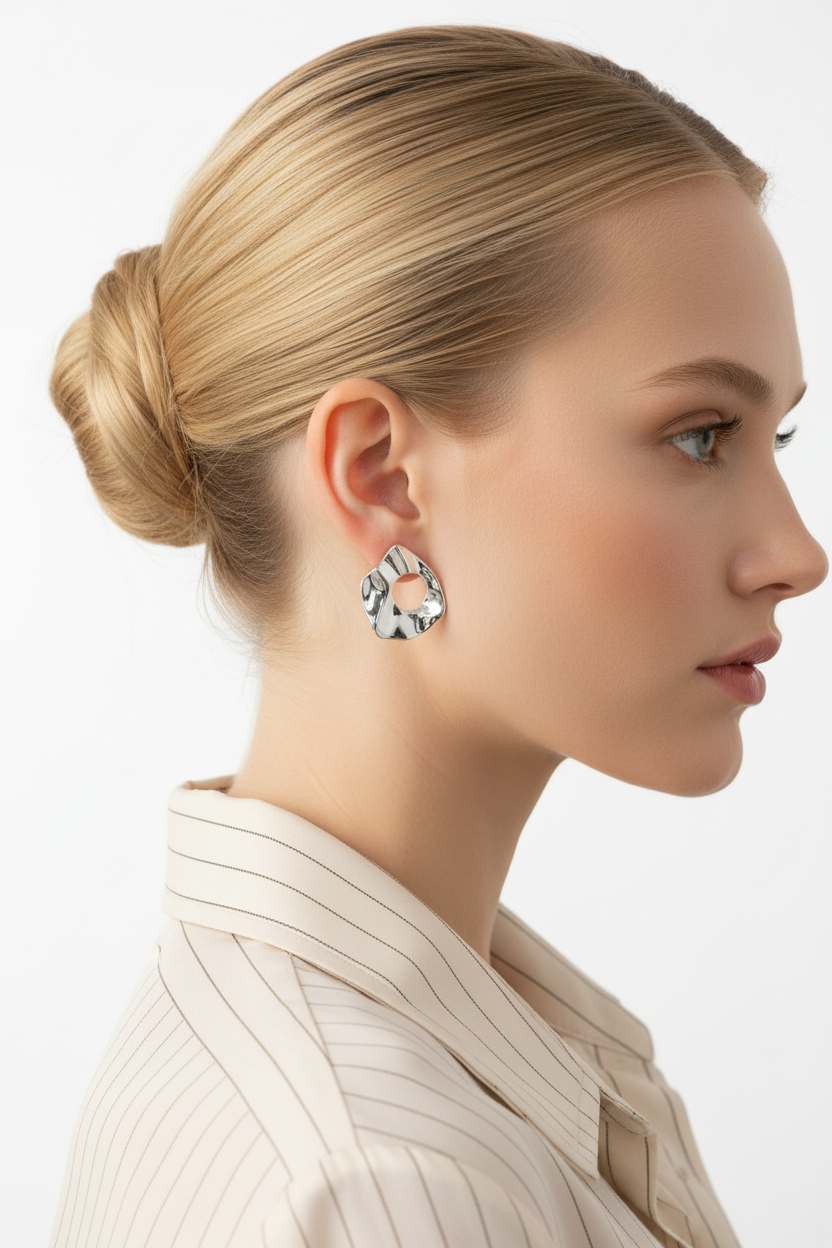 Blonde woman with ballerina bun wearing silver irregular waterdrop stud earrings, white background