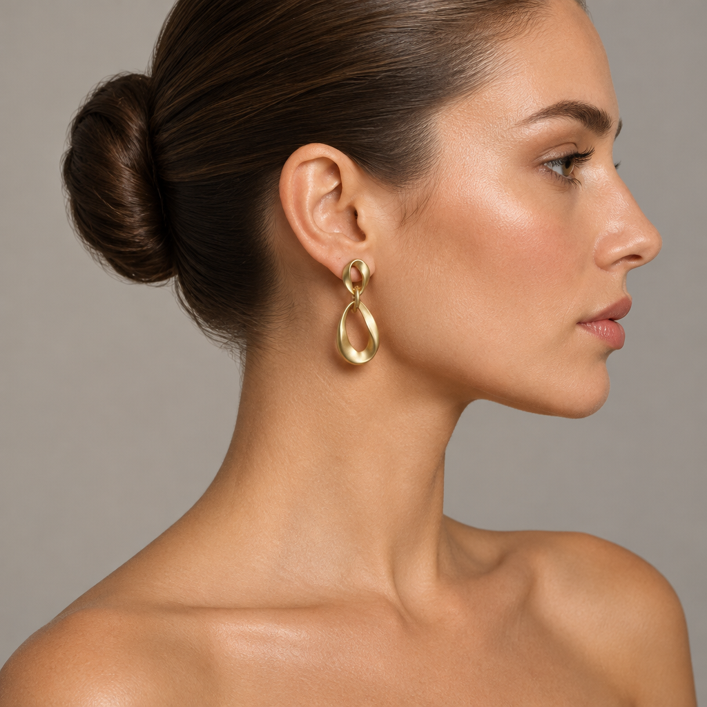 Side profile of a woman with a ballerina bun wearing a matte gold-tone geometric earring