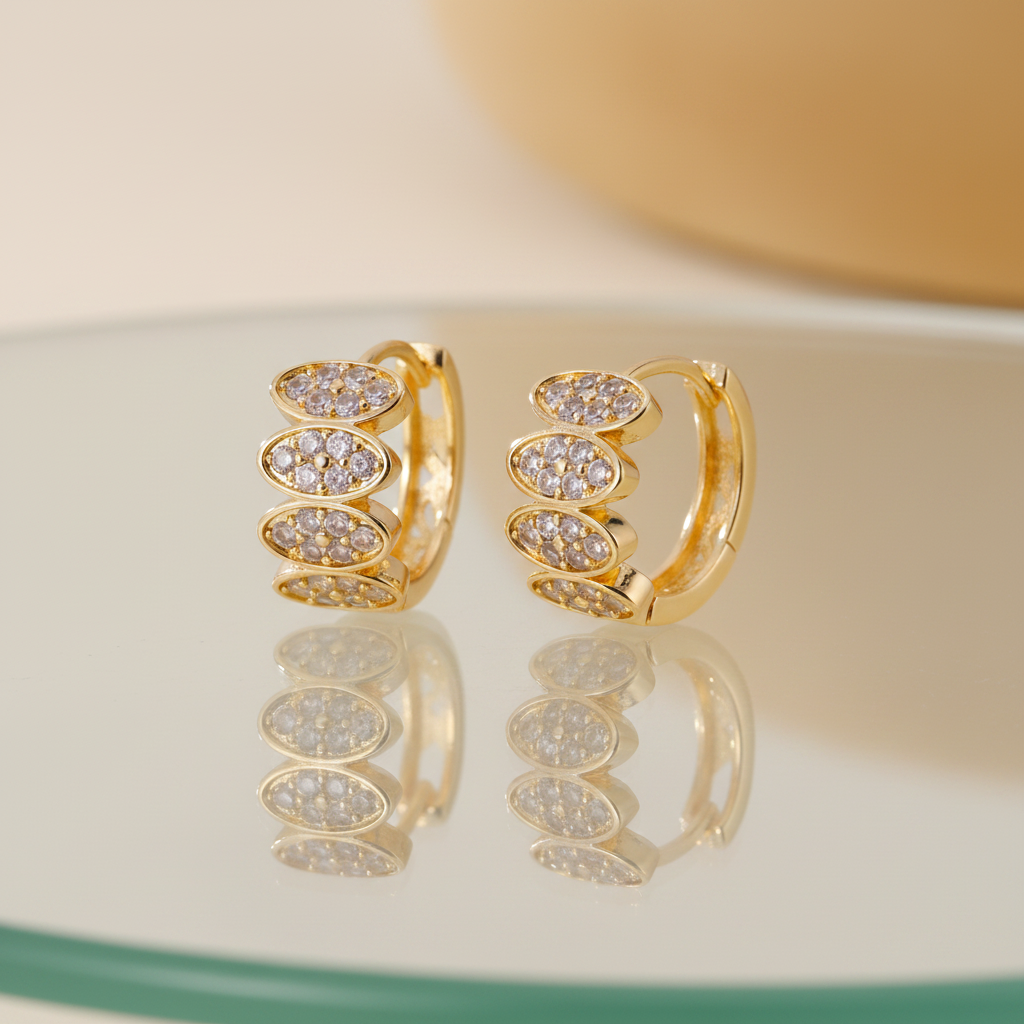 Gold zircon huggie earrings on glass table